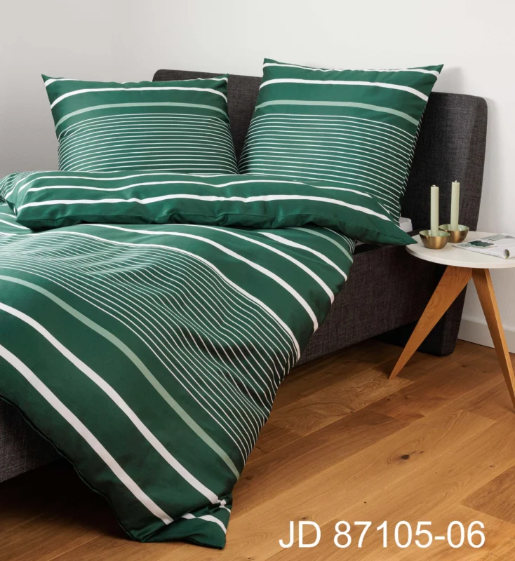 Janines J.D. Bettwäsche Mako-Satin 87105-06 Grün ziert ein dunkles Bett, gepaart mit einem kleinen hölzernen Beistelltisch mit Kerzen.